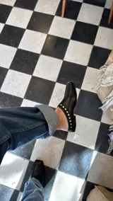 Mules de cuero negro con punta cuadrada y detalle de tachas plateadas en el borde superior.