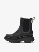 Bota tipo Chelsea de caña media confeccionada en cuero de oveja color negro. Presenta paneles elásticos laterales, tirador trasero con detalle tejido y suela chunky de goma con relieve.