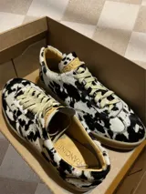 Zapatillas bajas con estampado animal print de vaca en blanco y negro, con cordones marrones y suela color caramelo.