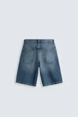 Bermuda de denim de algodón, color gris claro lavado, de corte ancho (baggy fit) y largo hasta la rodilla. Presenta cinco bolsillos y cierre frontal con cremallera y botón.