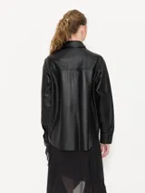 Camisa negra de cuero ovino con broches forrados en el mismo cuero, remaches con brillo en el delantero y cuello, y bolsillos con vista de cuero en el delantero.