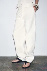Pantalón de tiro medio confeccionado en hilatura de algodón color blanco. Cuenta con trabillas en la cintura, bolsillos laterales ocultos en costura y cierre frontal con cremallera, botón y ganchos metálicos.