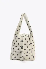 Bolso tipo bowling color crudo con estampado de lunares negros. Tiene doble asa de mano y correa bandolera extraíble. Incluye bolsillo interior con cremallera y cierre principal con doble cremallera.