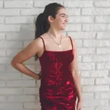 Vestido de terciopelo color borgoña, con escote recto, tiras finas regulables, espalda descubierta y falda ajustada con frunces laterales.