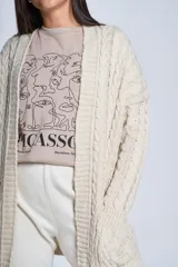 Saco tejido color crema con diseño de ochos y bolsillos frontales.