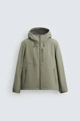 Cazadora verde oliva de tejido técnico con interior de forro polar. Tiene cuello con capucha ajustable, manga larga, bolsillos con cremallera en pecho y cadera, bajo ajustable con elástico y cierre frontal con cremallera.