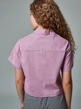 Camisa corta de lino color lila con cuello clásico, cierre frontal con botones, mangas cortas y dos bolsillos de parche en el pecho.