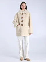 Chaqueta reversible de piel de oveja color crema con botones cuadrados de cuero marrón y bolsillos delanteros.