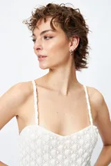 Top blanco de encaje con breteles finos, corte en la cintura y abertura frontal.