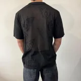 Camisa negra tejida con diseño calado, corte regular, cuello tipo polo y cierre frontal con botones.