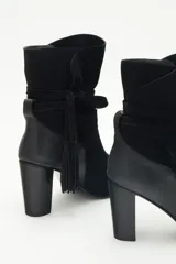 Botas de caña media de gamuza negra, con taco cuadrado y punta fina. Presenta tiras terminadas con borlas que se cruzan y atan alrededor de la caña.