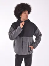 Campera con capucha color gris oscuro, con paneles superiores en tela lisa y paneles inferiores en tela tipo sherpa. Cierre frontal con cremallera y bolsillos laterales.