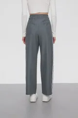 Pantalón gris de calce ancho y tiro alto, con bolsillos laterales y apliques de dos líneas blancas verticales en los laterales.