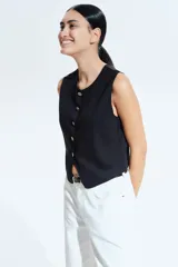 Chaleco negro de punto con cuello redondo y cierre frontal con botones dorados.
