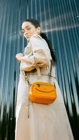 Bandolera naranja de cuero sintético con bolsillo frontal con cierre y bolsillo pequeño con tapa y broche magnético. Cuenta con apertura central superior con cierre, bolsillos internos y correa larga regulable y desmontable.