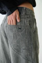 Pantalón jean gris de tiro medio con calce amplio, bolsillos delanteros y traseros, recortes en las piernas, trabillas para cinturón y cierre con botón y cremallera.