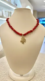 Collar corto de cuentas redondas de nácar color rojo, con dije colgante dorado en forma de rama de coral.