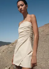 Minivestido strapless color beige con textura de rayas diagonales, diseño drapeado y cierre lateral invisible.