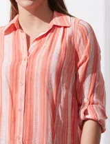 Camisa larga de rayón marca Robert Louis, con estampado a rayas verticales en tonos coral y blanco. Tiene cuello con solapa, abertura central con botones, mangas largas regulables con presilla y botón, y tajos laterales.