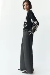 Pantalón negro de tiro alto con pinzas delanteras, pernera ancha y cinturón de cuero con hebilla dorada.
