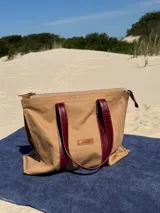 Bolso tipo tote de lona color beige con asas de cuero color bordó, cierre superior y bolsillo interno.