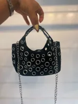 Cartera negra con múltiples ojalillos metálicos plateados y correa de cadena metálica plateada.