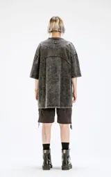 Remera de cuello redondo, calce oversize, color gris oscuro con efecto batik artesanal (acid wash). Presenta un corte curvo en la parte superior del pecho que simula un recorte.