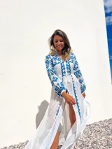 Túnica playera blanca traslúcida con bordados azules, mangas largas y abertura frontal.