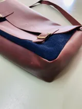 Maletín marrón de cuero y gamuza azul, con correa larga regulable y cierre con hebillas.