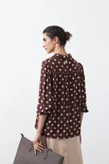 Camisa de manga larga color marrón con estampado de lunares blancos, confeccionada en tejido liviano con cuello clásico y botones frontales.