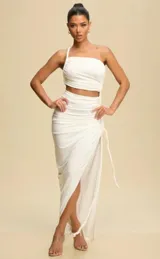 Vestido largo blanco de un solo hombro, con corte a la cintura y falda con abertura lateral y detalle de nudo ajustable.