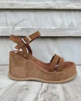 Sandalias de cuero color marrón con plataforma y taco de 8cm forrados en gamuza. Diseño con doble tira frontal y tira regulable al tobillo con hebilla metálica.