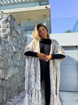 Ruana larga de lana merino color beige jaspeado, con diseño de trenzas y flecos en el borde inferior.