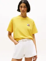 Remera amarilla de algodón con corte amplio, cuello redondo y hombros caídos. Presenta un logo pequeño de Tommy Hilfiger en el pecho, un logo en la manga y un logo grande en la espalda. Pertenece a la colección Hilfiger Sailing.