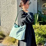 Bolso tipo tote color gris claro, con doble asa de mano y correa larga regulable. Tiene dos bolsillos laterales y un bolsillo frontal.