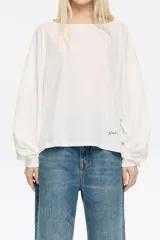 Camiseta de manga larga color crudo, con corte holgado, cuello redondo y pespuntes a contratono. Tiene un pequeño bordado con el logo de la marca en el frente.