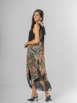Vestido midi negro con estampado tropical de hojas y flores en tonos tierra, naranja y verde. Es de tirantes anchos con nudo regulable en el hombro y tiene aberturas laterales.