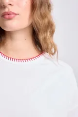 Remera blanca de corte holgado con cuello redondo y mangas cortas, terminaciones con pespunte rojo.
