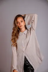 Camisa color beige claro, de corte holgado, con cuello clásico, cierre frontal con botones, mangas largas con puños abotonados y detalles de broderie en la parte delantera.