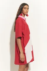 Túnica corta de mangas cortas con cuello camisero y cierre frontal con botones. Presenta un diseño bicolor con una franja diagonal en color beige.