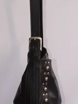 Bolso tipo bandolera de cuero negro con flecos y tachas plateadas. Tiene correa regulable, forro interior y bolsillo interno.