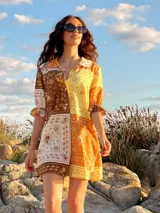 Vestido corto con estampado de cachemir en tonos marrones, amarillos y blancos. Tiene cuello camisero, mangas cortas con volantes y cierre frontal con botones.