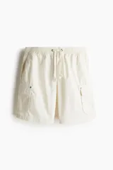 Short cargo color crema en popelina de algodón, con cintura elástica ajustable con cordón, bolsillos laterales y bolsillos con solapa y botones a presión en las piernas y atrás.