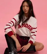 Suéter blanco de jacquard con letras 'Amour' en rojo y rayas horizontales rojas en las mangas.