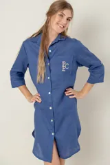 Vestido camisero azul de lino con mangas 3/4, cuello clásico, cierre abotonado frontal y bolsillo en el pecho con bordado de iniciales.