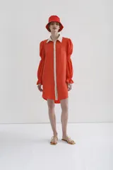 Vestido camisero corto color naranja, con cuello y cartera en contraste color crema, manga larga abullonada con puños elásticos y cierre frontal con botones.