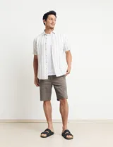 Camisa de manga corta a rayas verticales celestes y blancas, con cuello clásico y botones marrones.