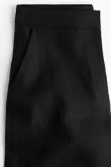 Pantalón negro de corte ancho, tiro alto, con bolsillos al bies y cierre oculto.