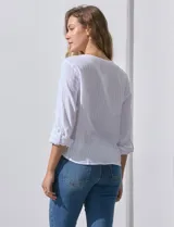 Blusa de algodón a rayas verticales finas en tonos blanco y lila, con escote en V, abertura frontal con botones y mangas largas regulables con presilla y botón. El ruedo termina anudado al frente.