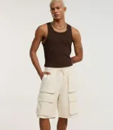 Bermuda baggy color crema, confeccionada en algodón y poliéster. Cuenta con cintura elástica ajustable con cordón y bolsillos cargo laterales.